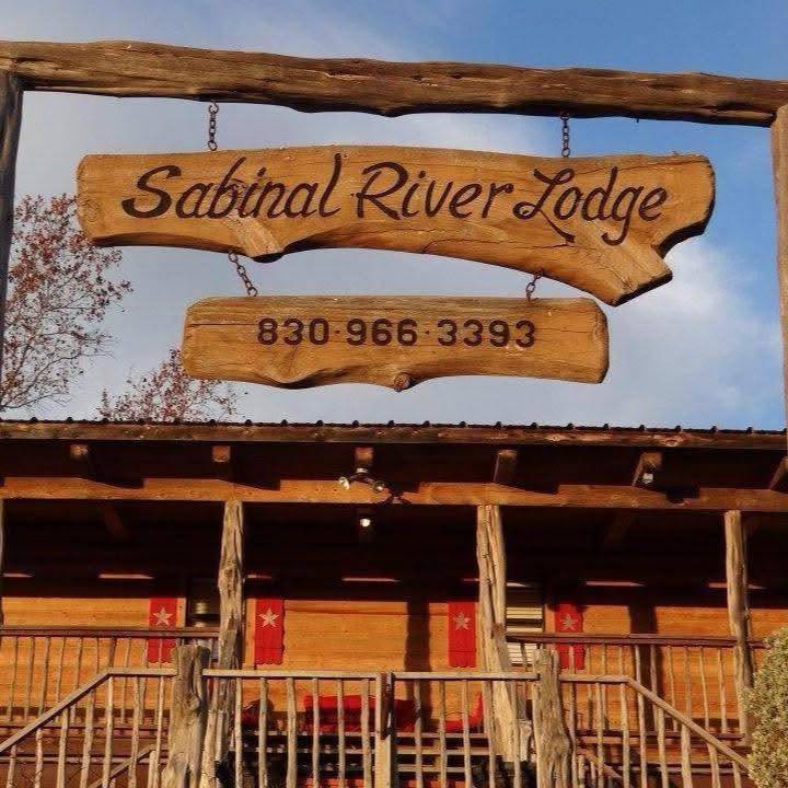 Sabinal River Lodge wooden entrance sign with phone number 830-966-3393, hanging above the lodge's covered porch in Utopia, Texas